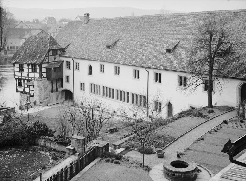 Un jardin et les bâtiments d’un couvent vus d’en haut. Sur les toits, il y a des tuiles plates. L’enduit des murs a été refait récemment. Le jardin a été réaménagé. Photo en noir et blanc.